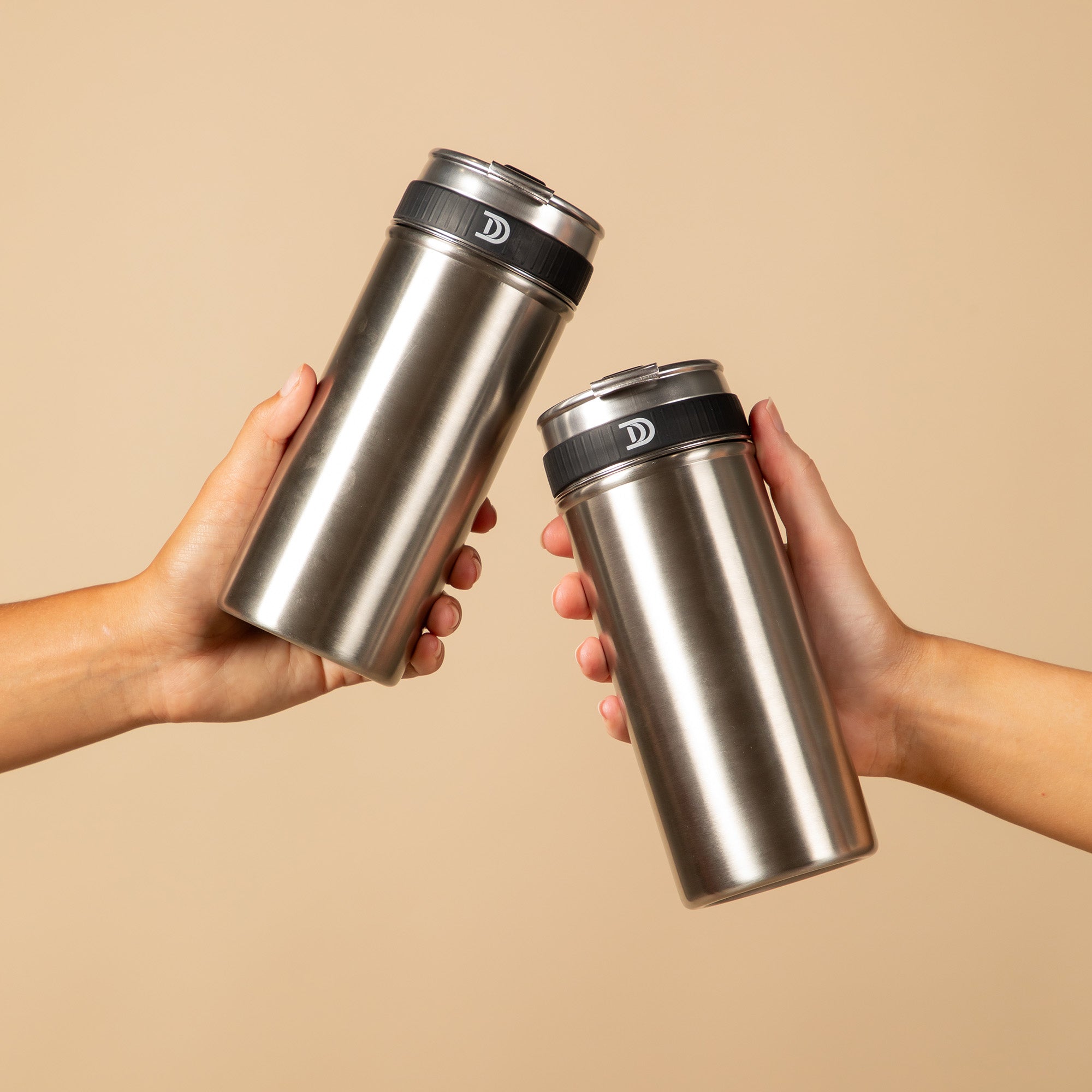 Two hands holding Devoted Steel Shakers, 100% plastic-free stainless steel gym shaker against a beige background.